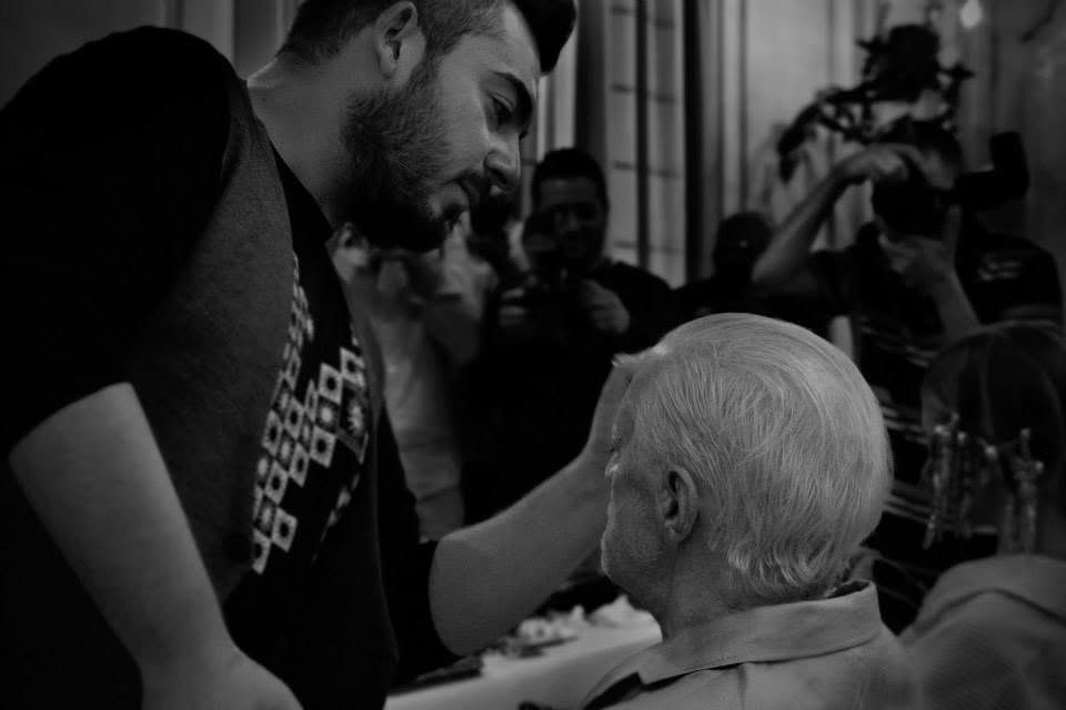 Antonio Lagani trucca un uomo anziano sul set, tra fotografi e luci