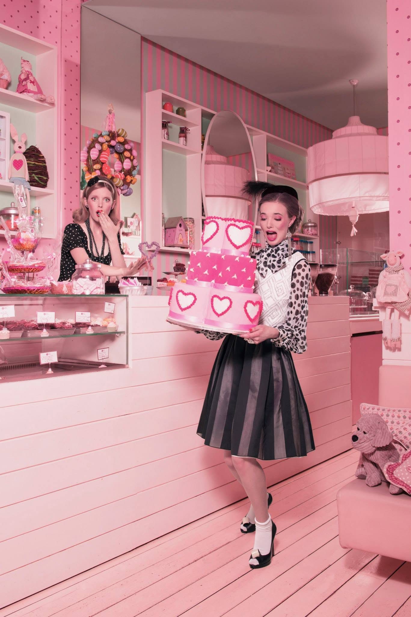 Editorial in una pasticceria rosa: modella con torta a cuori, trucco e styling anni Cinquanta