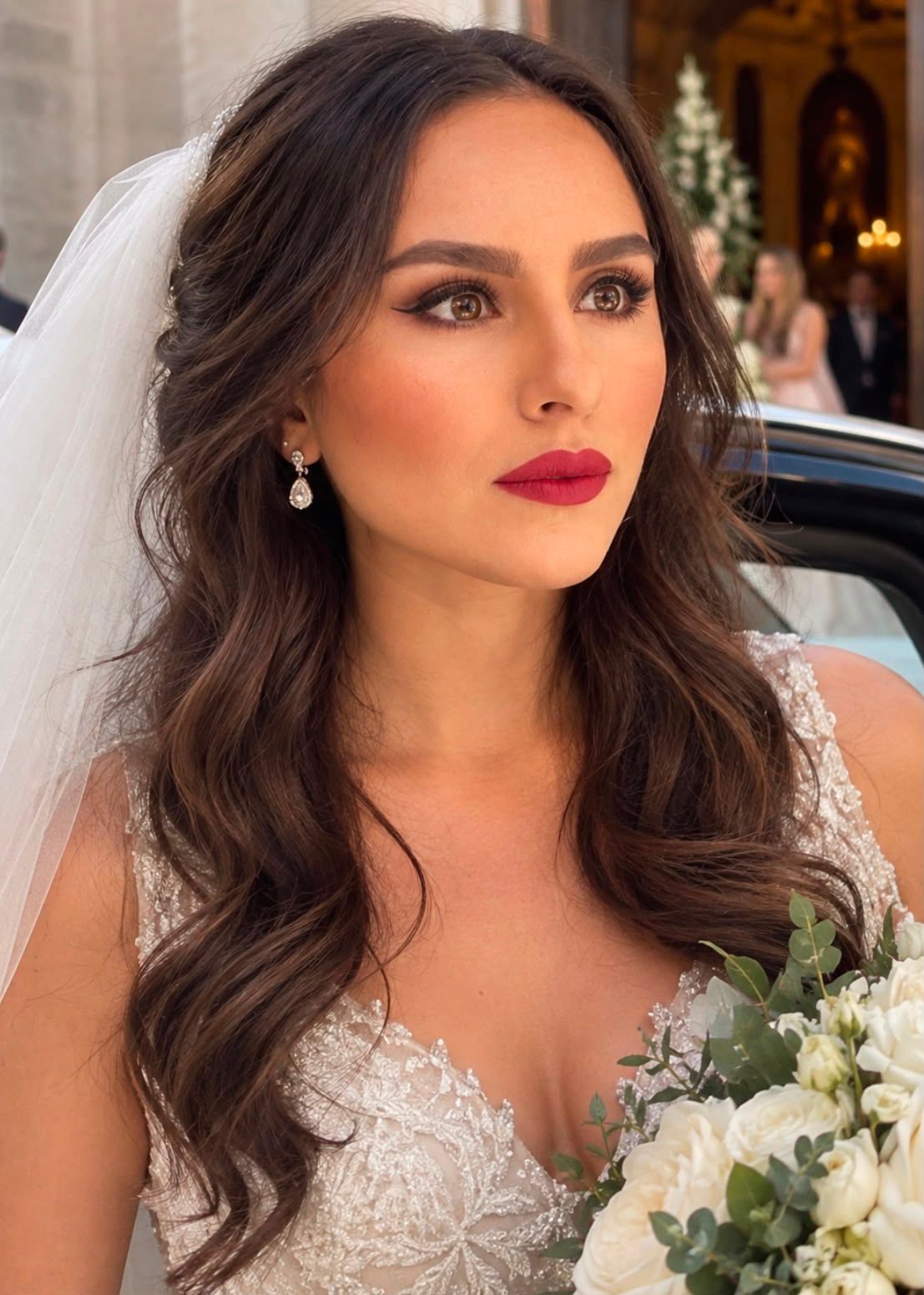 Sposa all'uscita dalla chiesa con velo e bouquet di rose bianche, eyeliner deciso e labbra rosse opache